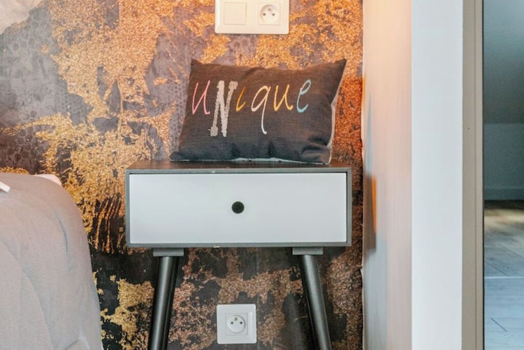 A white bedside table with a unique pillow against a textured wall.