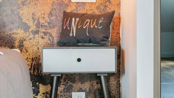 A white bedside table with a unique pillow against a textured wall.