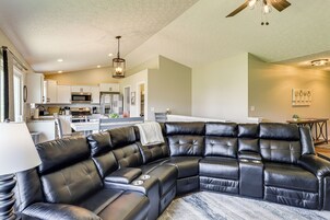 A modern living room with a black leather sectional sofa, a dining area, and a kitchen in the background.
