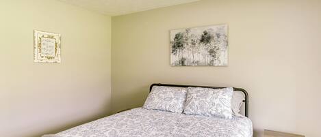 A bedroom with a bed, a nightstand, a wall-mounted picture, and a ceiling with a textured pattern.
