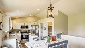 A modern kitchen with white cabinetry, stainless steel appliances, and a dining area with a table and chairs. - Deck & Outdoor Dining: Family Getaway in Dry Ridge (Dry Ridge)