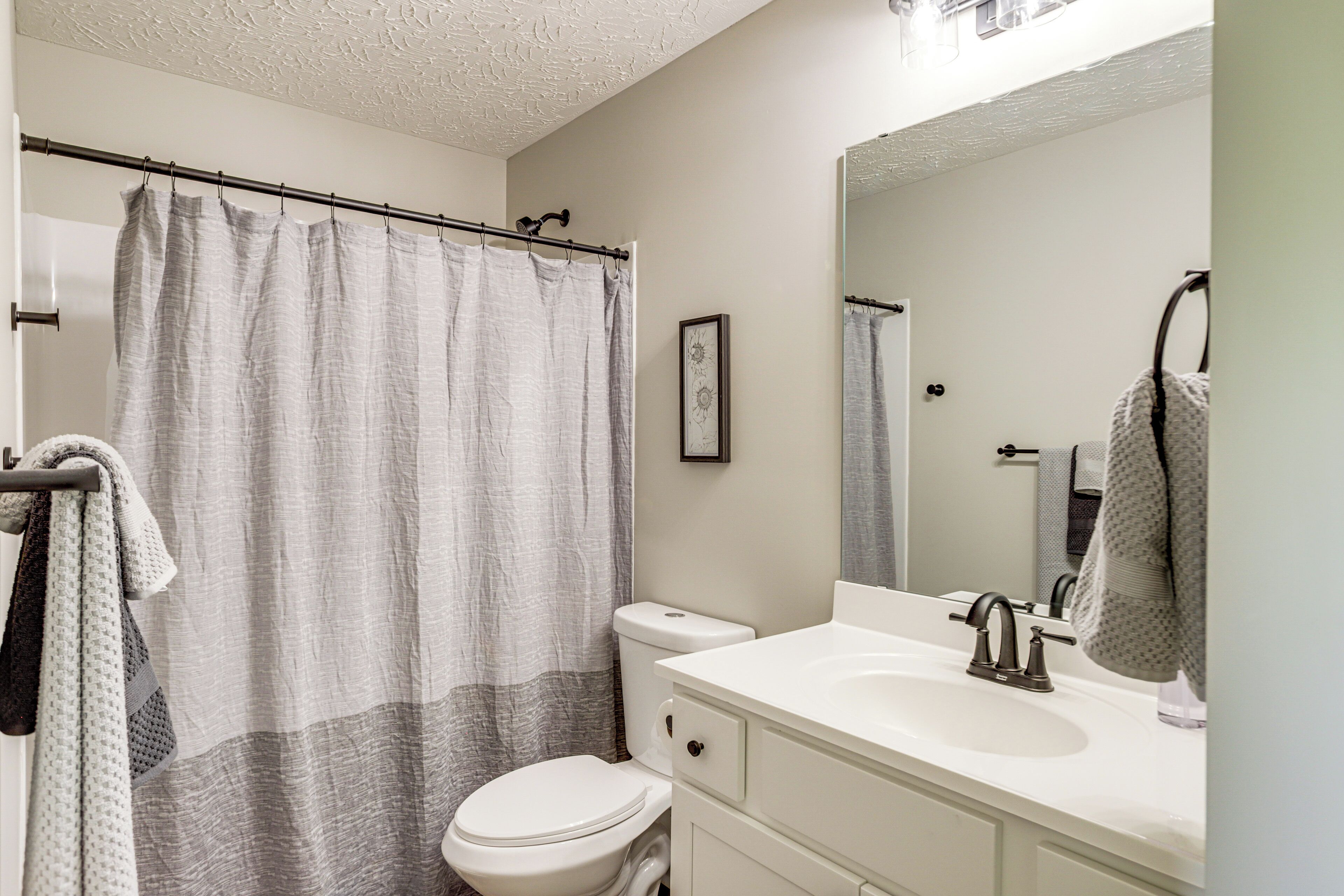 A bathroom with a shower curtain, toilet, sink, and mirror.