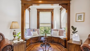 A cozy bay window seating area with a wooden bench, a small table, and a lamp. - Spacious Home Chef's Kitchen, BBQ Grill, 5 Min Cle Clinic, Hot Tub, ADA, King (Cleveland)