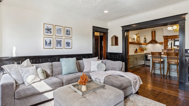 A living room with a grey sofa, a coffee table with a tray and vase, and a kitchen visible through an open doorway. - Spacious Home Chef's Kitchen, BBQ Grill, 5 Min Cle Clinic, Hot Tub, ADA, King (Cleveland)