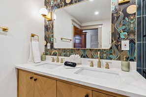 Ein Badezimmer mit zwei Waschbecken, einem großen Spiegel und einer Wandverzierung.