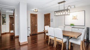 A dining area with a wooden table, white upholstered chairs, and a modern pendant light.