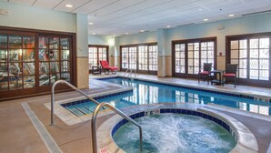 An indoor swimming pool with a hot tub, lounge chairs, and a glass-enclosed area with exercise equipment.
