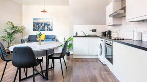 Eine moderne Küche mit weißen Schränken, einer schwarzen Arbeitsplatte und einem eingebauten Backofen. Es gibt eine Essecke mit einem runden Tisch und schwarzen Stühlen.