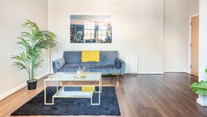 Ein Wohnzimmer mit einer Couch, einem Couchtisch, einer Topfpflanze und einem Stadtbild an der Wand.