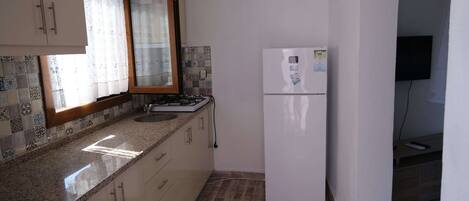 A kitchen with a white refrigerator, a stove, and a window with a curtain.