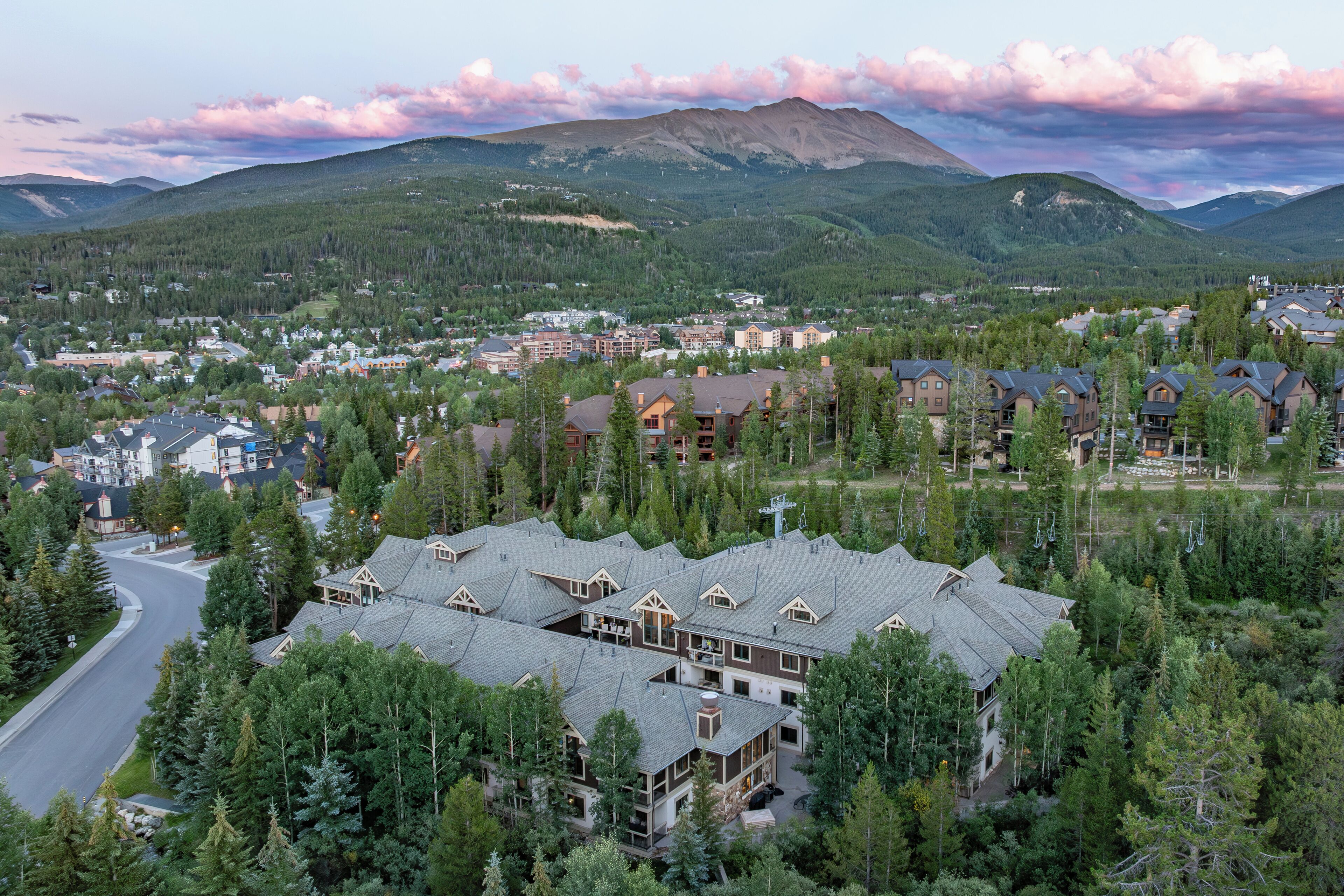 A lodge with multiple floors, surrounded by dense forest, with a mountain in the background.