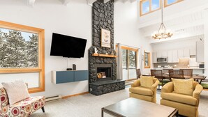 A spacious living room with a stone fireplace, comfortable seating, a flat-screen TV, and a kitchen area visible through an open door. - Central, Top Floor Unit, Close to Lift and Town (Breckenridge)