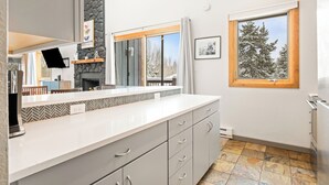 A modern kitchen with a stone accent wall, a large window with a view of snow-covered trees, and a built-in oven. - Central, Top Floor Unit, Close to Lift and Town (Breckenridge)