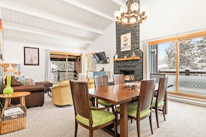 A spacious living room with a fireplace, dining area, and large windows offering a view of snow-covered trees. - Central, Top Floor Unit, Close to Lift and Town (Breckenridge)