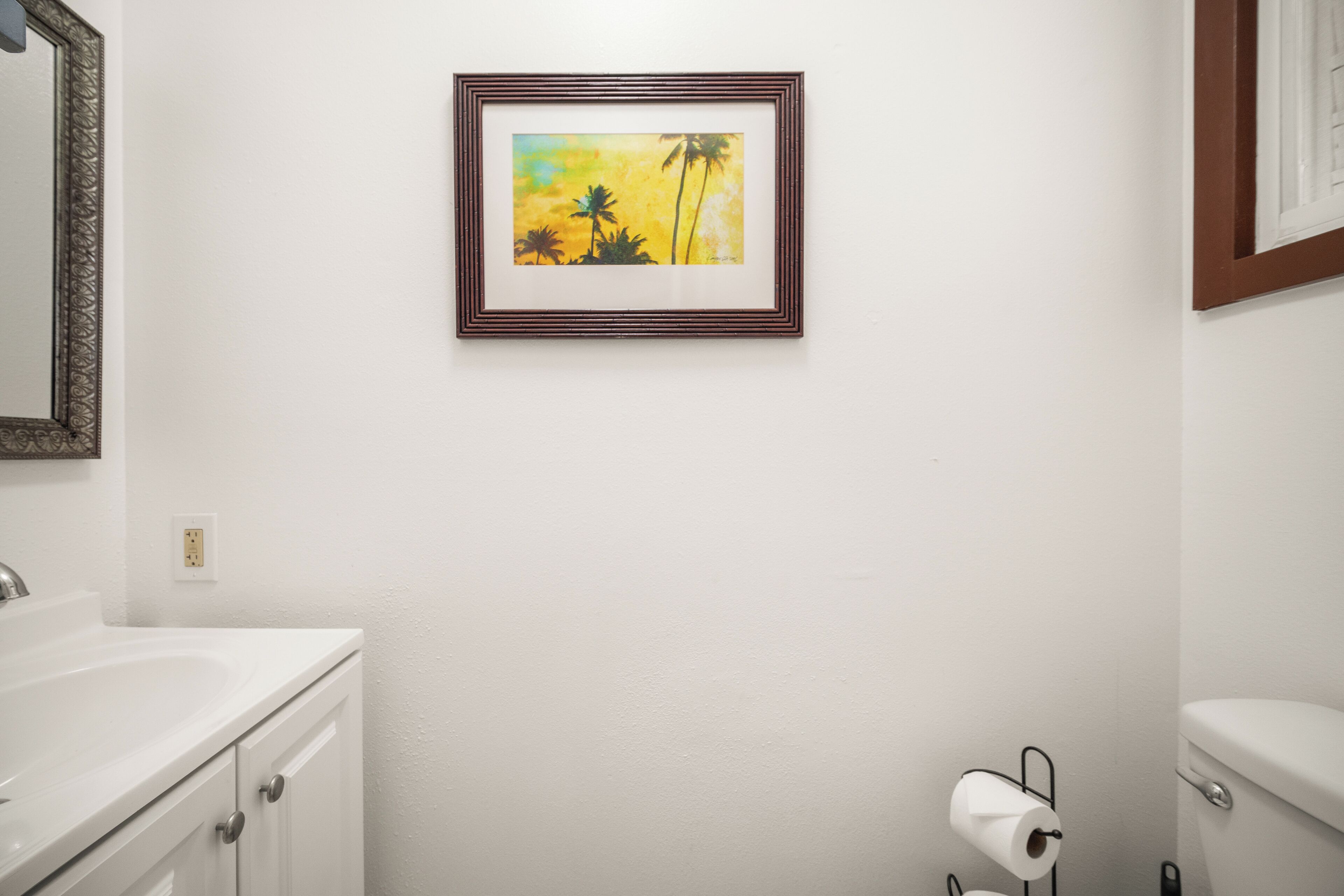 Een badkamer met een witte wastafel, toilet en een lijst met een kunstwerk aan de muur.