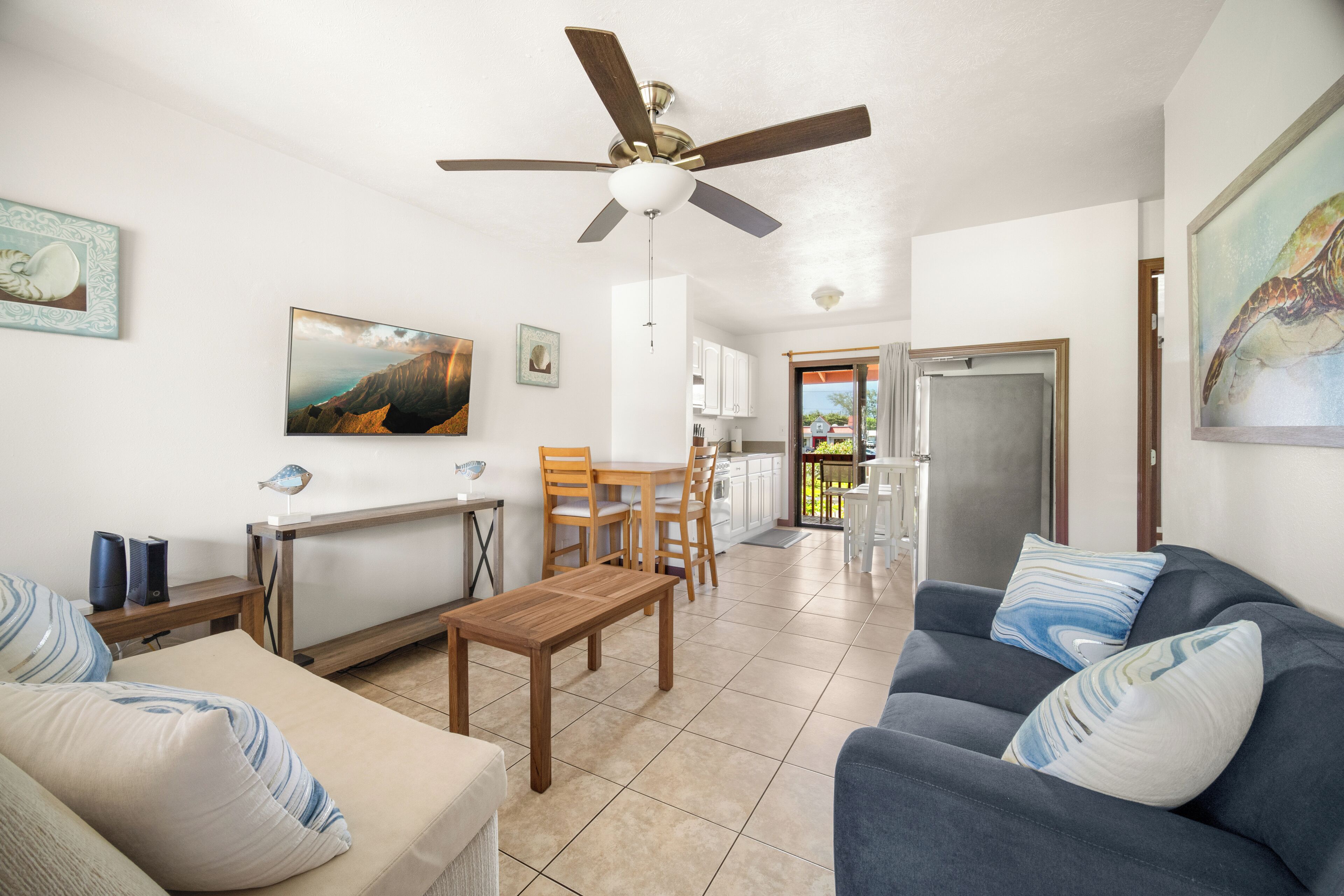 Ein geräumiger Wohnbereich mit Deckenventilator, einem Esstisch mit Stühlen, einer Couch und einer Küche im Hintergrund.