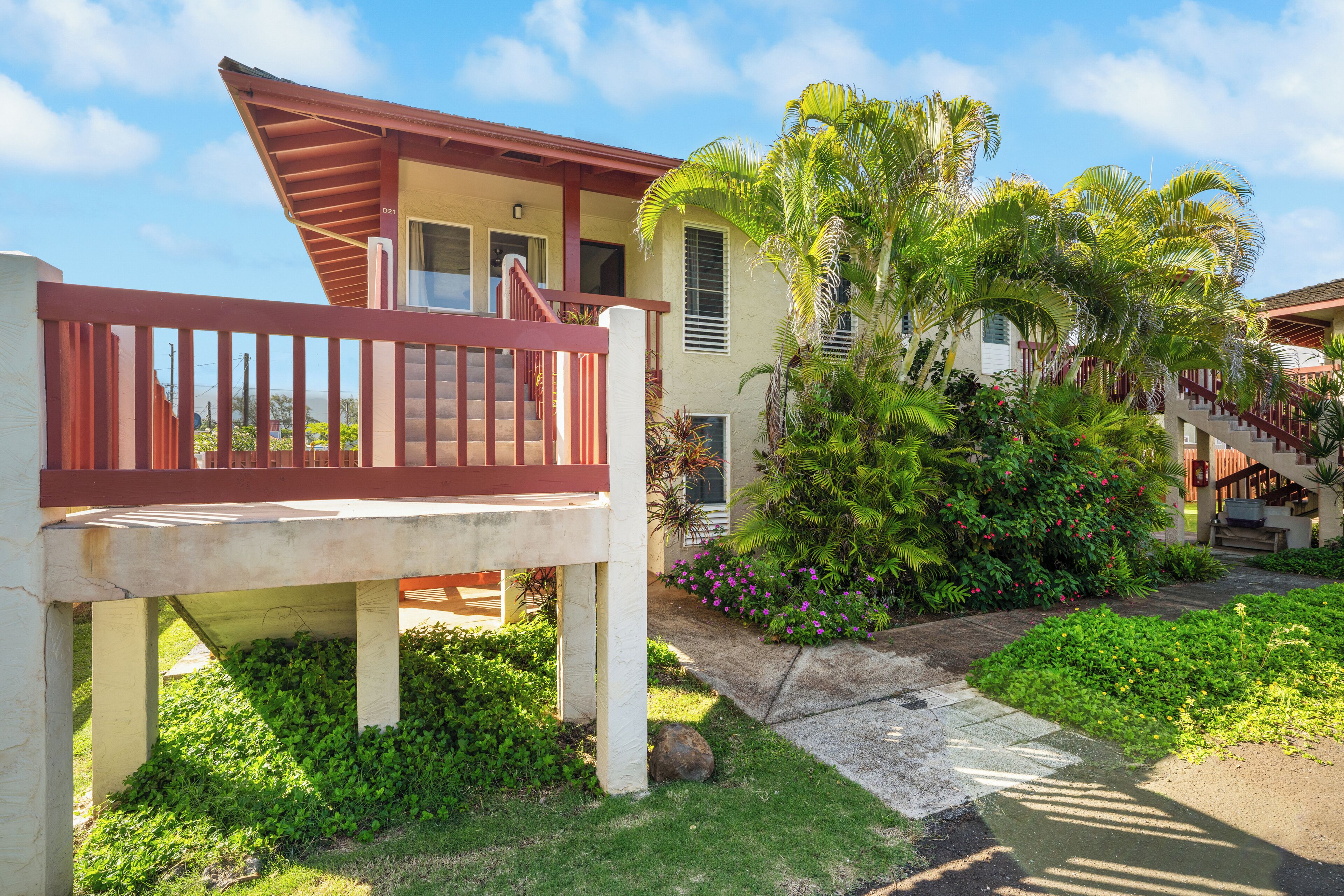 A two-story building with a red balcony, surrounded by lush greenery and palm trees.