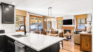 A modern kitchen with a large island, a dining area with a fireplace, and a living room with a TV. - On Main St. Hot Tubs, Easy Access to Peak 9. (Breckenridge)