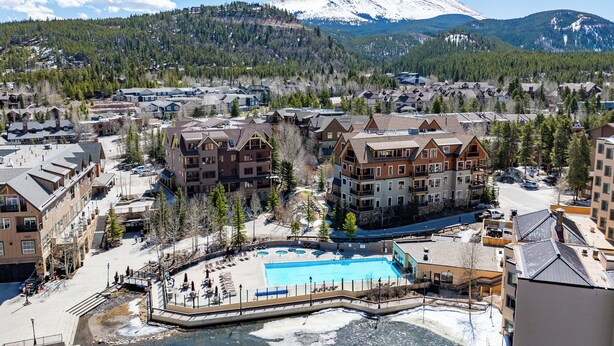 A resort area with multiple buildings, a swimming pool, and a view of snow-capped mountains. - On Main St. Hot Tubs, Easy Access to Peak 9. (Breckenridge)