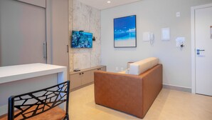 A modern hotel room with a reception desk, a seating area, and a large window with a view of the sea. - Elegance Residence (Bombinhas)