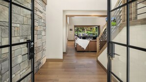 Un pasillo con una pared de piedra en un lado y una puerta de cristal en el otro, que conduce a un comedor con mesa y sillas.