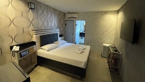 A modern hotel room with a large bed, a bedside table, a TV, and a bathroom visible through an open door. - Hotel Estrela Carapicuiba (Carapicuiba)