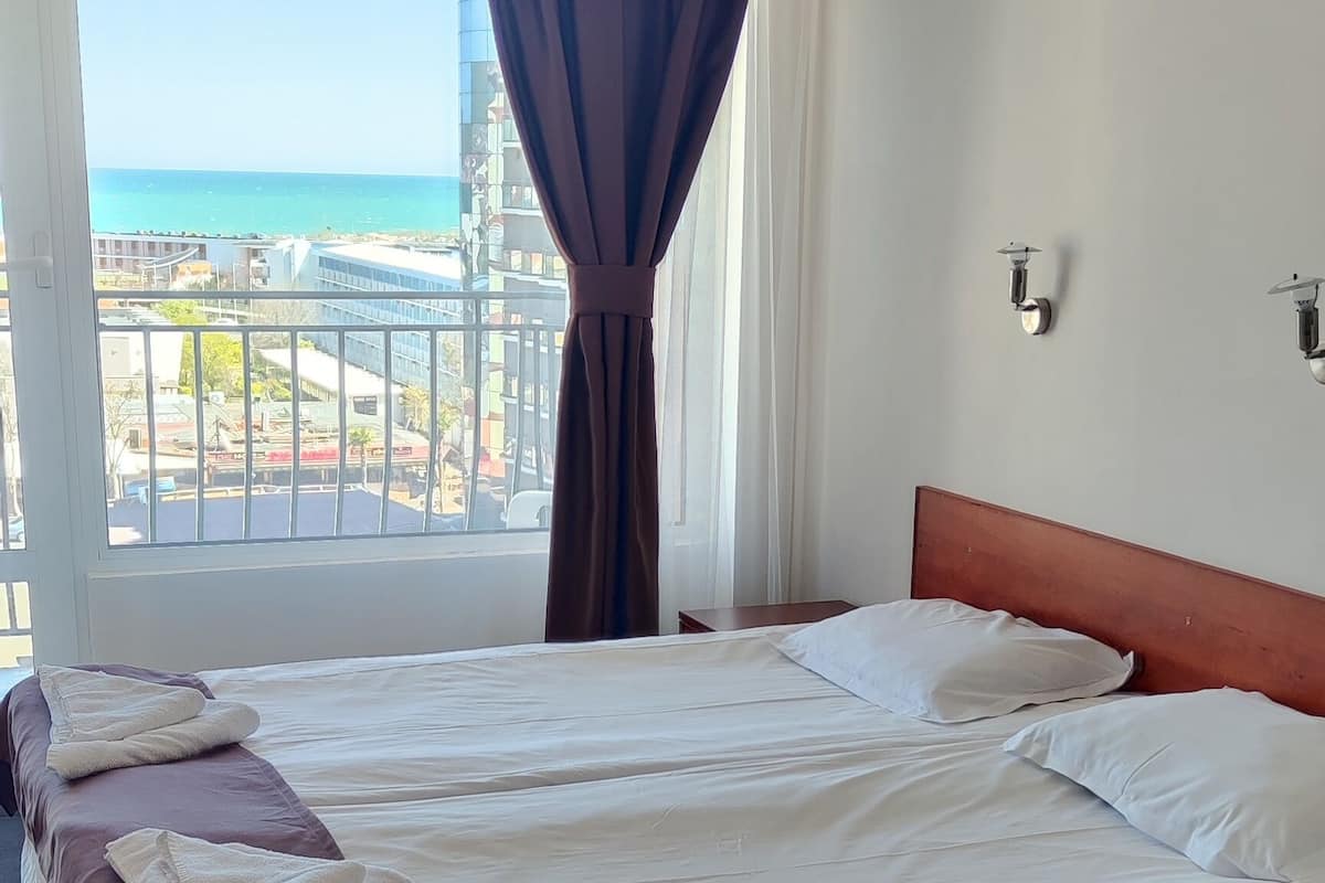 A hotel room with a large bed, a view of the sea, and a balcony.