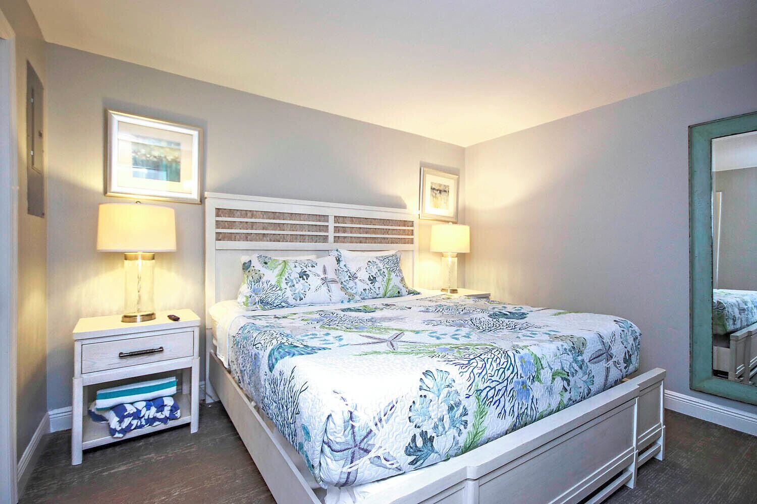 A bedroom with a bed, nightstands, a drawer unit, and a mirror.