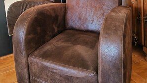 A brown leather armchair in a room with a wooden cabinet, a mirror, and pampas grass decorations.