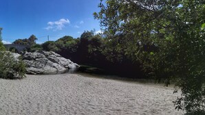 A sandy beach with a rocky outcrop and dense foliage.