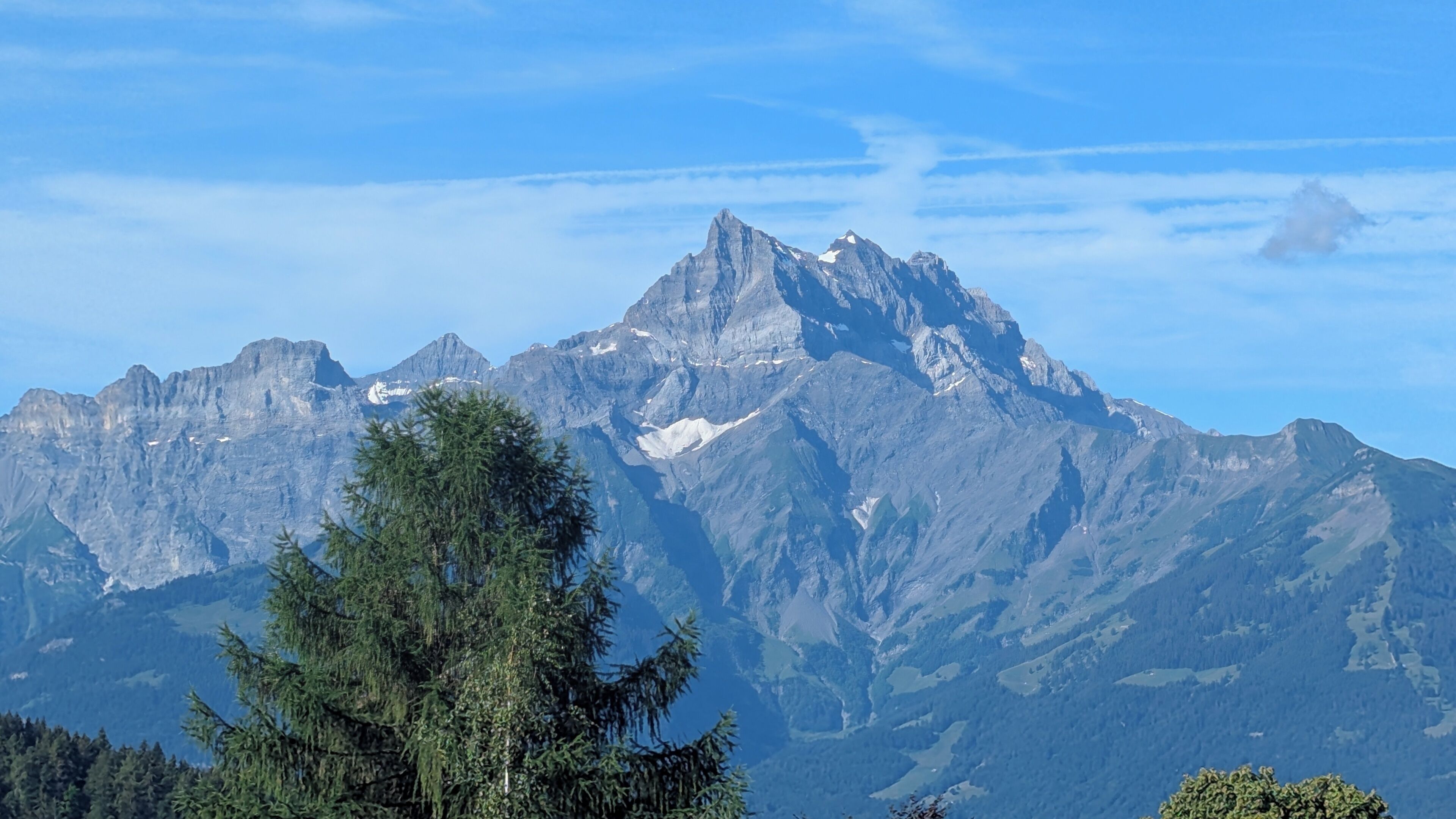 Ein Gebirgszug mit einem markanten Gipfel, dichter Vegetation im Vordergrund und blauem Himmel.