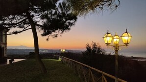 Un espace extérieur aménagé pour la nuit, avec une clôture en bois, un lampadaire et une vue sur le coucher de soleil sur l’eau.