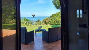 Vue depuis une pièce dotée d'une grande porte cintrée donnant sur un patio extérieur aménagé avec des meubles en osier et offrant une vue sur la mer.