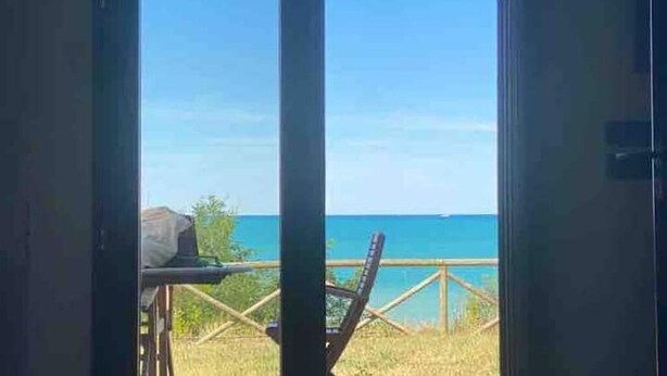 Vue depuis l’intérieur d’une pièce dotée d’une grande fenêtre donnant sur une plage et l’océan.