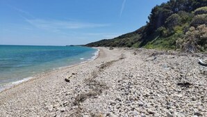 Une plage de galets bordée d’une eau d’un bleu limpide et d’une colline boisée.