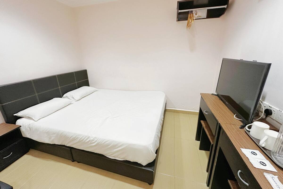 Ein Hotelzimmer mit Bett, Fernseher, Schreibtisch inklusive Computer und einer kleinen Ablage mit Uhr.