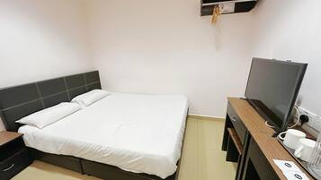 Habitación de hotel con cama, televisor, escritorio con computadora y una pequeña repisa con un reloj.