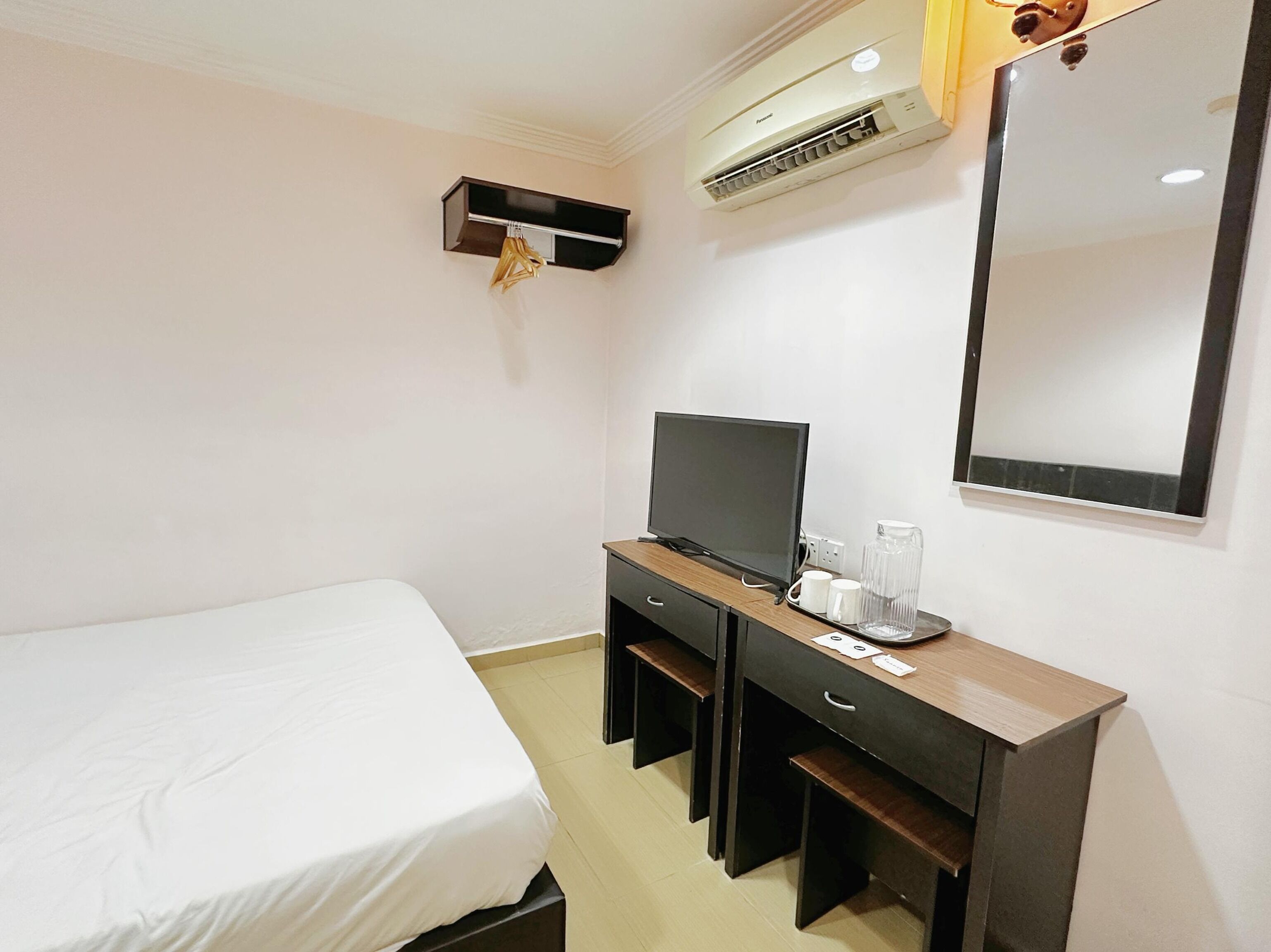 A hotel room with a bed, a desk with a television, a mirror, and an air conditioning unit.