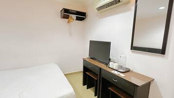 A hotel room with a bed, a desk with a television, a mirror, and an air conditioning unit.