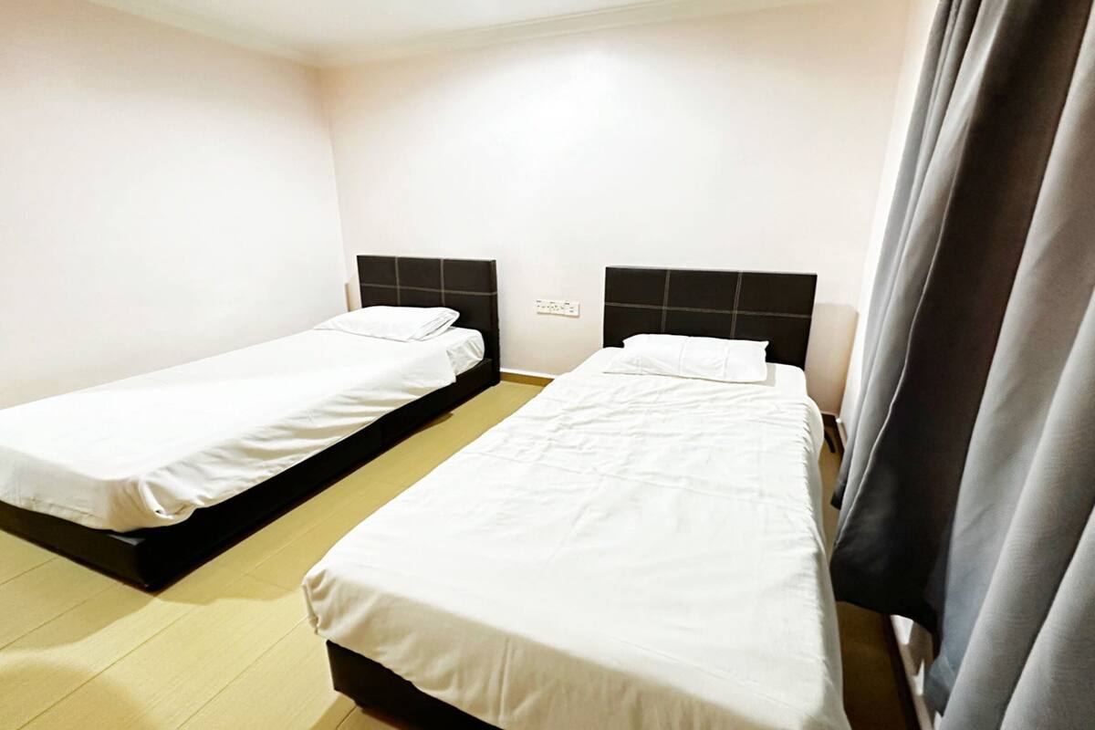 Zwei Einzelbetten mit schwarzen Kopfteilen in einem Zimmer mit weißen Wänden und Holzboden.