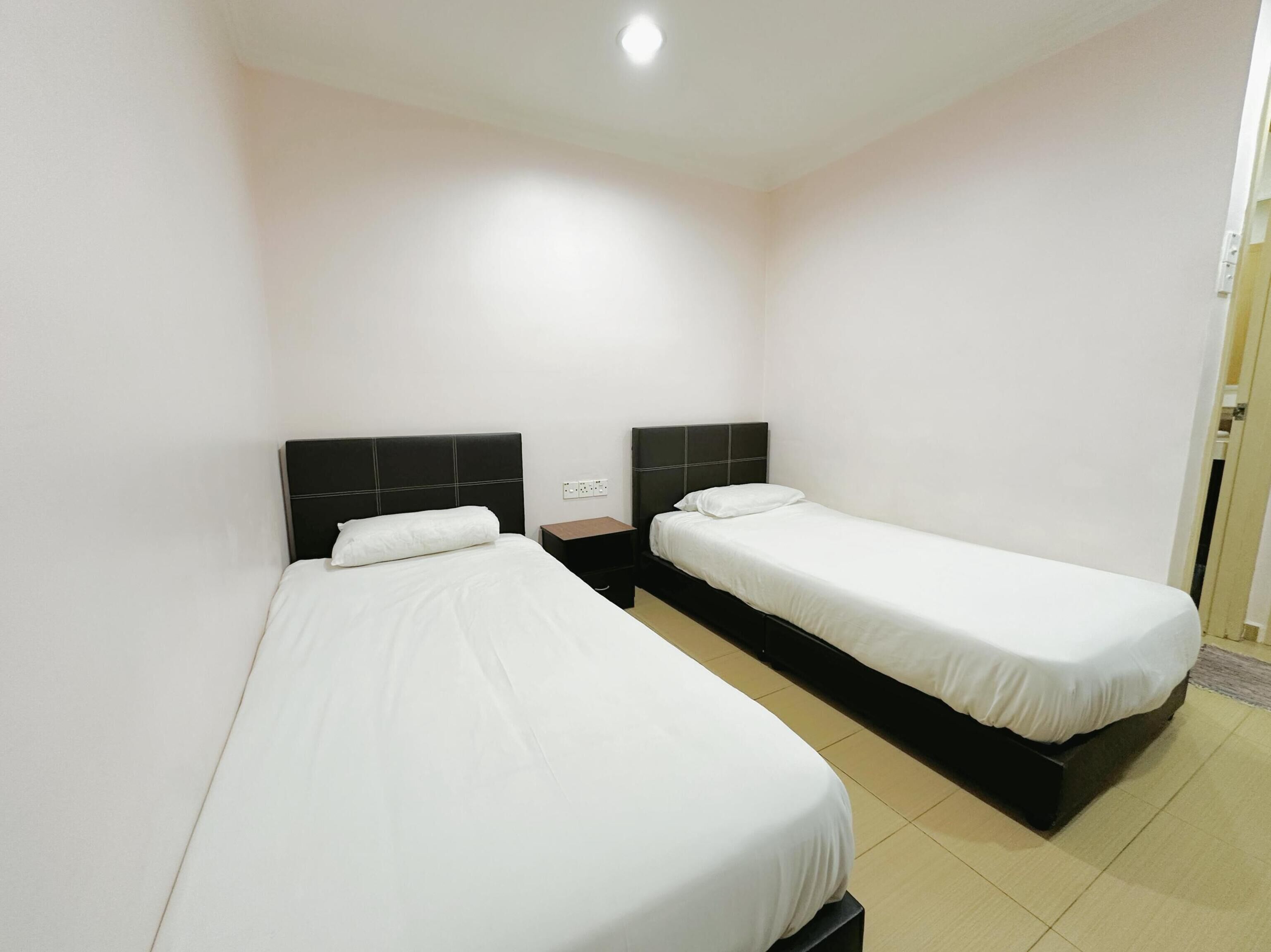 A hotel room with two single beds, a small bedside table, and a power outlet on the wall.