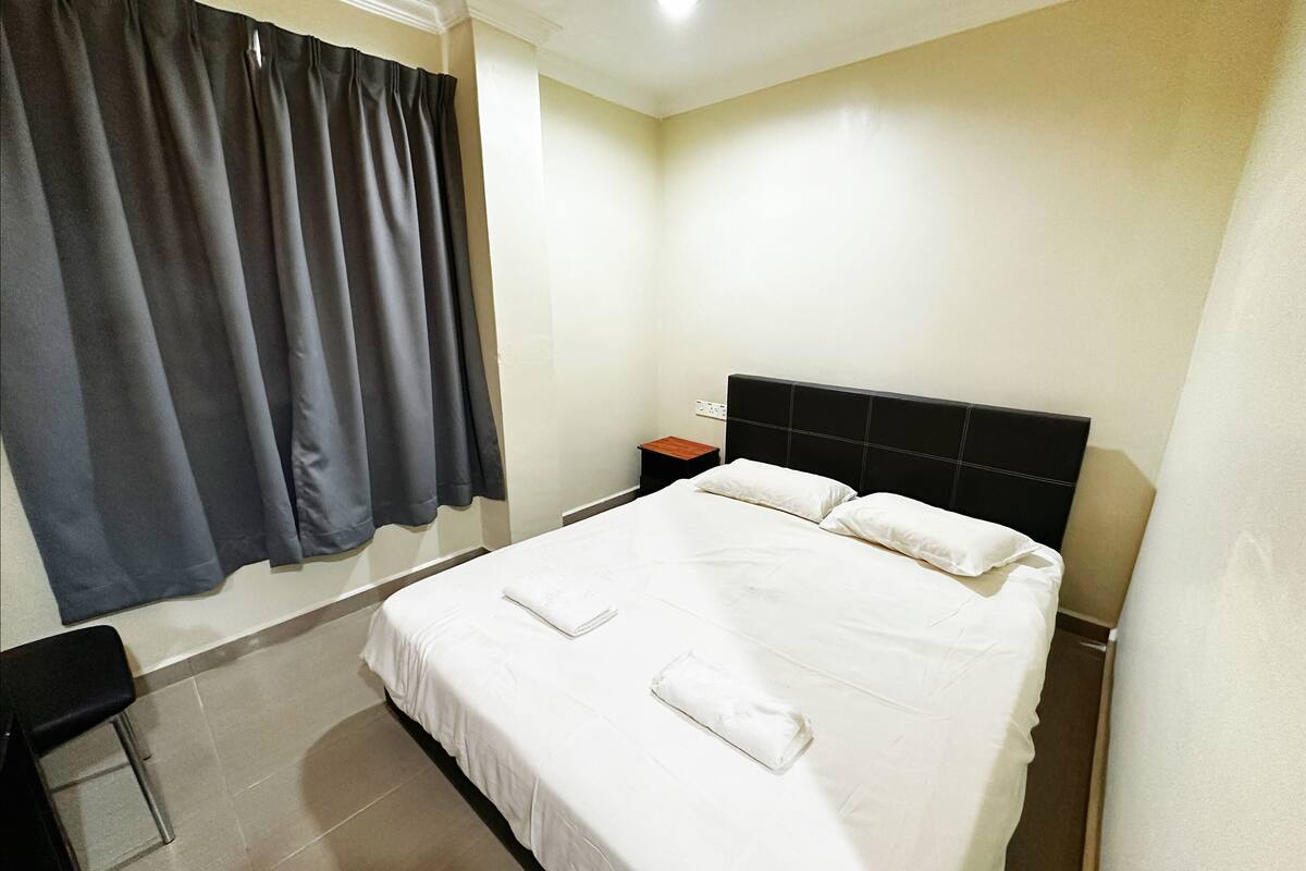 Ein Hotelzimmer mit einem großen Bett, einem Nachttisch, einem Stuhl und einem Fenster mit Vorhängen.