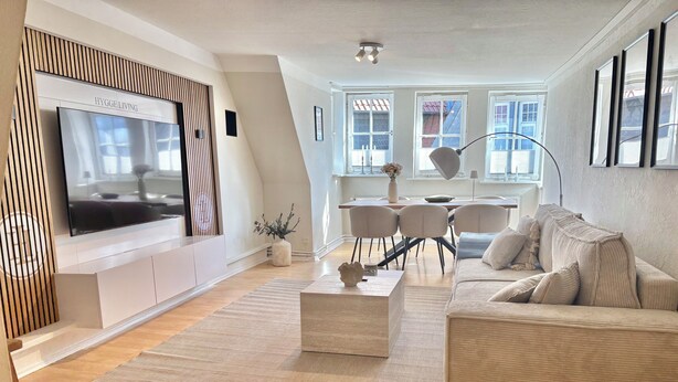 A modern living room with a large flat-screen TV, a sofa, a coffee table, and a dining area with chairs and a table. - HyggeLiving | 94m² | view of Marktkirche | OSCAR (Goslar)