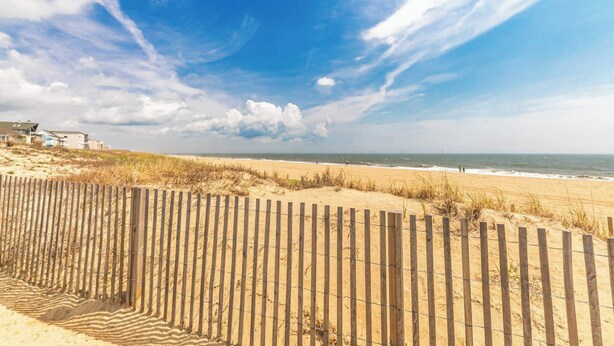 Ein Strand mit Holzzaun, Sanddünen und blauem Himmel.