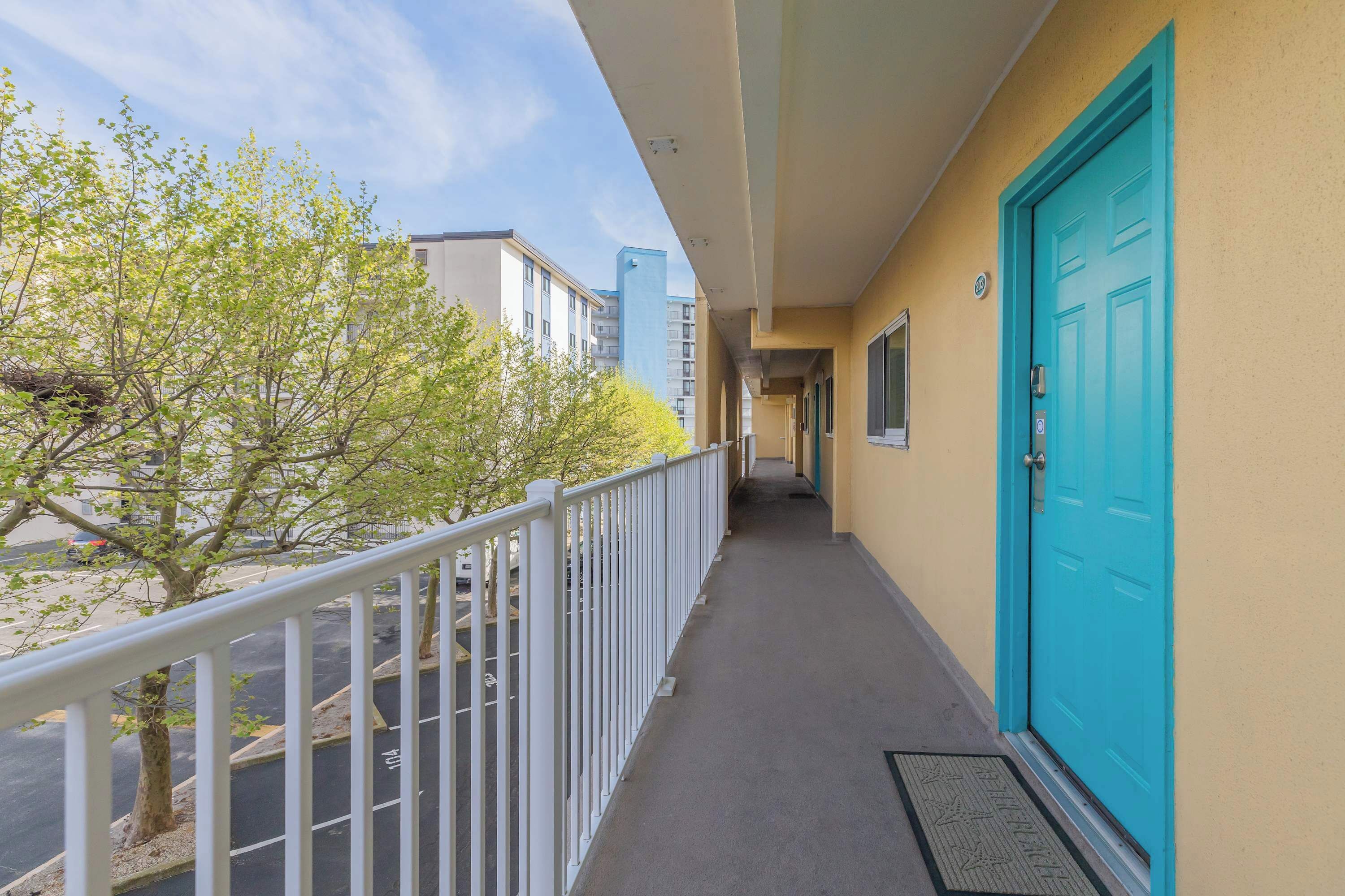 Een balkon met een witte reling, een turquoise deur en uitzicht op gebouwen en bomen.