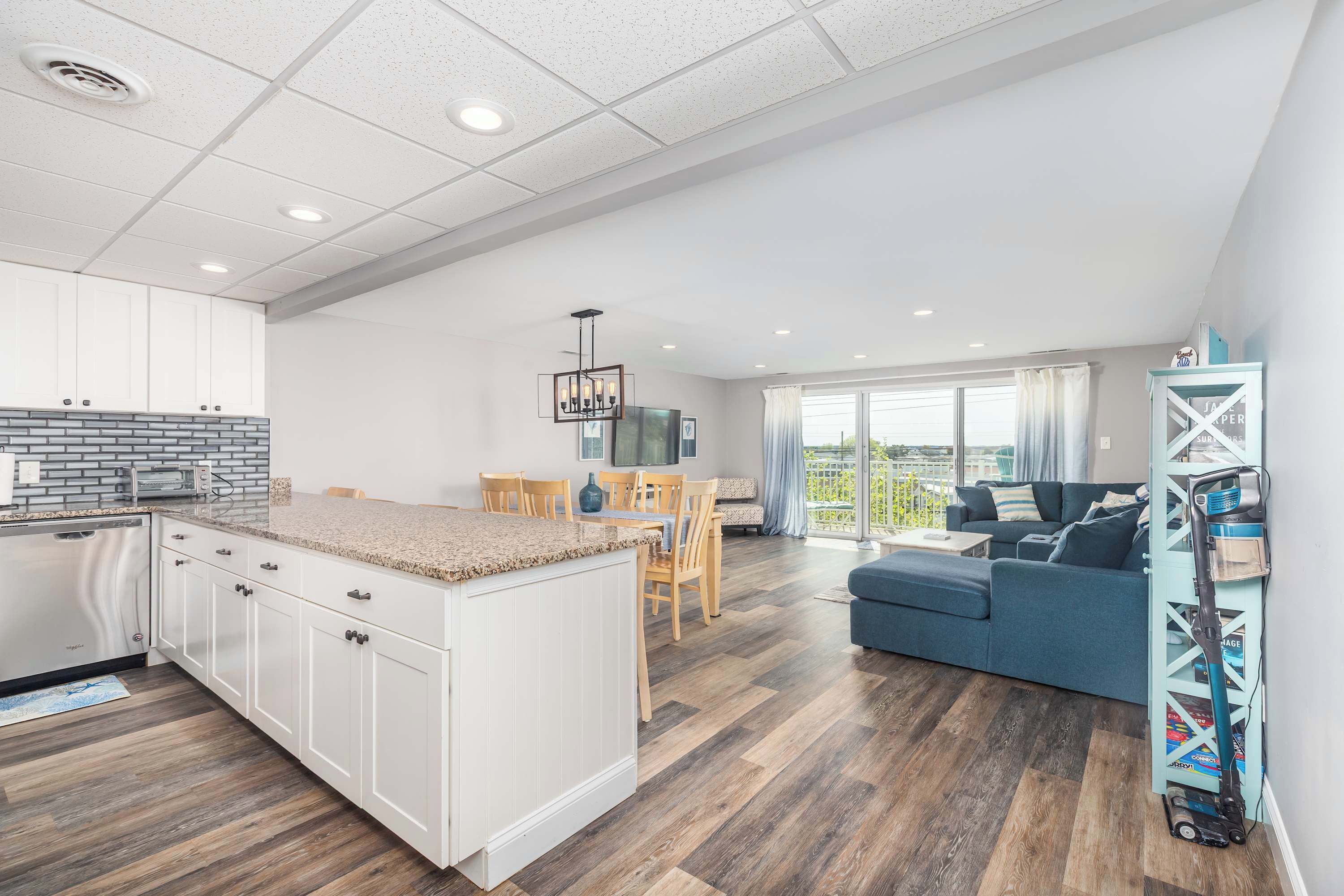 A modern kitchen with white cabinets, a granite countertop, and a dining area with wooden chairs.