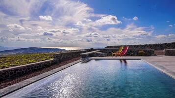 A swimming pool with a stone wall and colorful chairs, overlooking a landscape with mountains and a body of water.