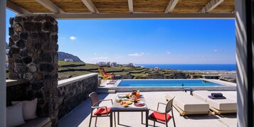 Terraza con piscina, mesa de comedor y sillas con vista a un paisaje costero.