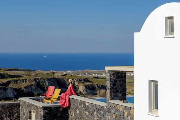 A coastal view with a pool, a white building, and two lounge chairs.