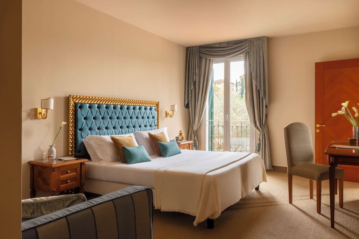 A hotel room with a large bed, a nightstand, a chair, a desk, and a view of the outdoors.